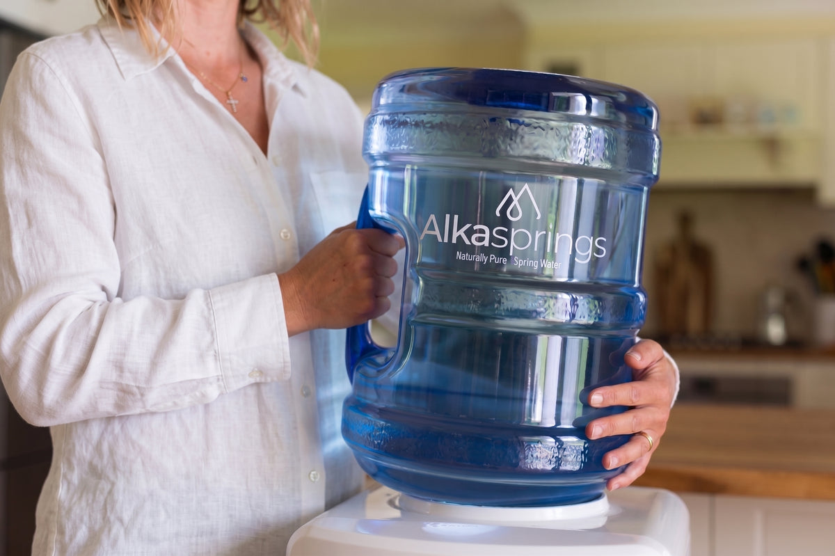 A woman placing an Alkasprings water bottle on a ceramic dispenser
