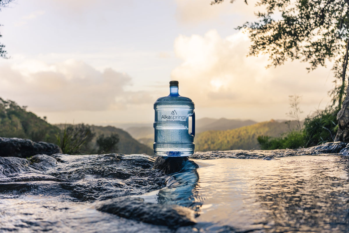 Alkasprings spring water bottle beside a stream with mountains in the background