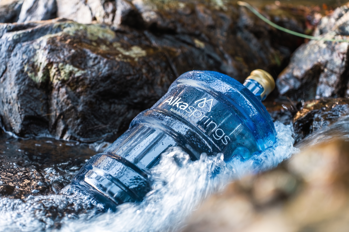 Alkasprings spring water bottle among rocks in a flowing stream